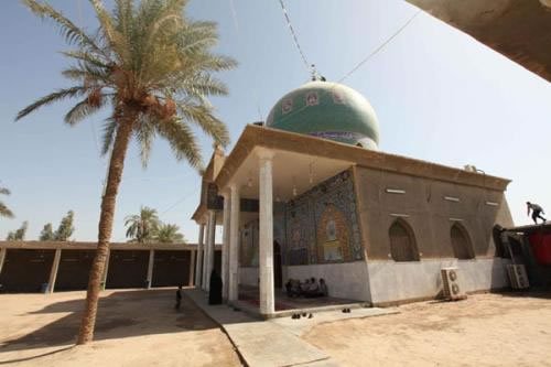 Job's shrine in Babel, Iraq.<br><br>The image shows the Tomb of Prophet Ayub (Job), a sacred shrine located near the city of Hillah in the Babylon Governorate of Iraq.Revered by Muslims, Christians, and Jews alike, the site honors the biblical prophet renowned for his legendary patience and steadfast faith through immense personal suffering. The architectural complex features a prominent green dome adorned with traditional Arabic calligraphy, a columned portico with intricate mosaic tilework, and a sandy courtyard lined with palm trees. According to local historical traditions, the site also features a sacred spring or well believed to have been used by the prophet for healing during his long illness.